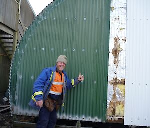 A man gives a ‘thumbs up’ in front of the Nissen hut