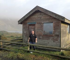 A man stands outside a wooden hut on the isthmus