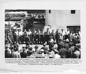 A group of men stand in front of a crowd at a wharf