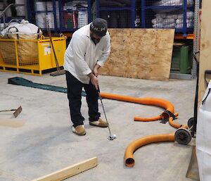 A man trying to putt the ball into an orange pipe