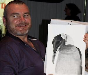 A man holds up a picture of a penguin.
