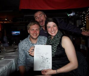 A man and woman holding up a message, with a man pulling a face behind.