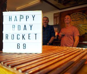 A happy birthday sign in front of 2 men