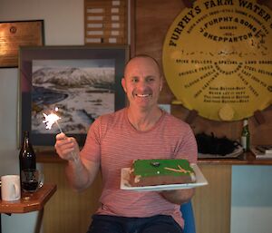 A man holds a cake and sparkler