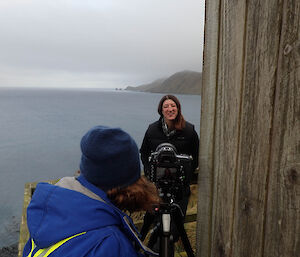 A woman is being interviewed on a balcony above the sea