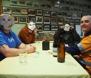 4 people sitting around a table with 3 in animal face masks