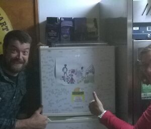 A man and a woman give a picture on the fridge the thumbs up