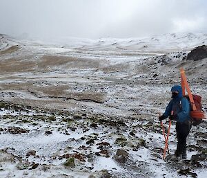 A man stands on the snowy plateau with a pack full of track markers