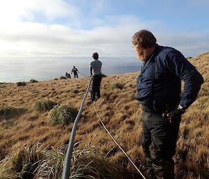 A pipe and line go down a hill with men working alongside it