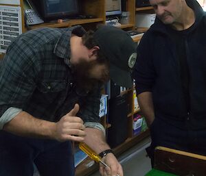 One man working on the pool table while another watches.