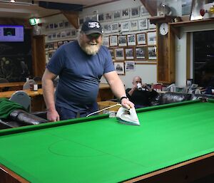 A man irons the felt of a pool table