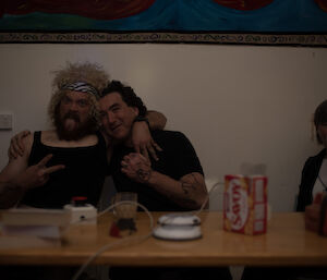 3 people at a table — 2 of the men pulling rock’n'roll faces