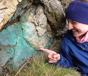 An expeditioner pointing at a rock that has blue looking dye coming down it