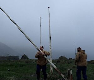 Two men taking down a flag pole ready to paint it
