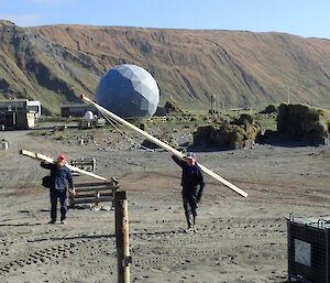 Two men carrying flagpoles across the isthmus