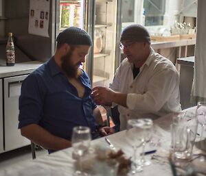 Two men trying to remove something from a shirt buttonhole