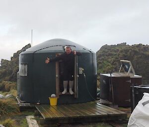 A man stands in front of the water tank hut.