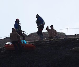 A group of men lowering the stretcher over the edge