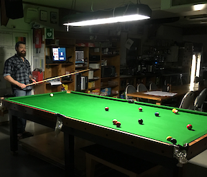 An expeditioner playing pool ponders his next shot across the green landscape