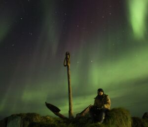 A lady sits on anchor rock under the aurora