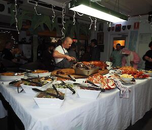 A table laden with food with the chef carving a spit pig