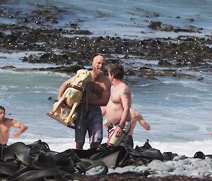 People getting out of the surf and back onto the beach. One man carrying a pretend guide dog called Stay Here