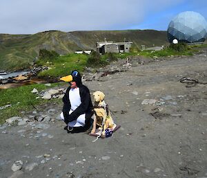 A man in a penguin suit with a dog statue on the beach
