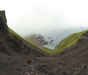 A man sits on a slope enjoying the view of the ocean