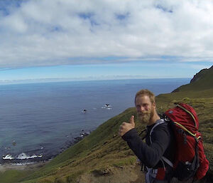 A man gives a thumbs up in front of a coastal view