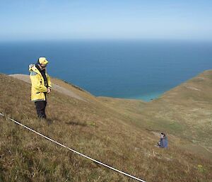 two people working on a site above Hidden Valley, they are standing amongst the vegetation with water in the background