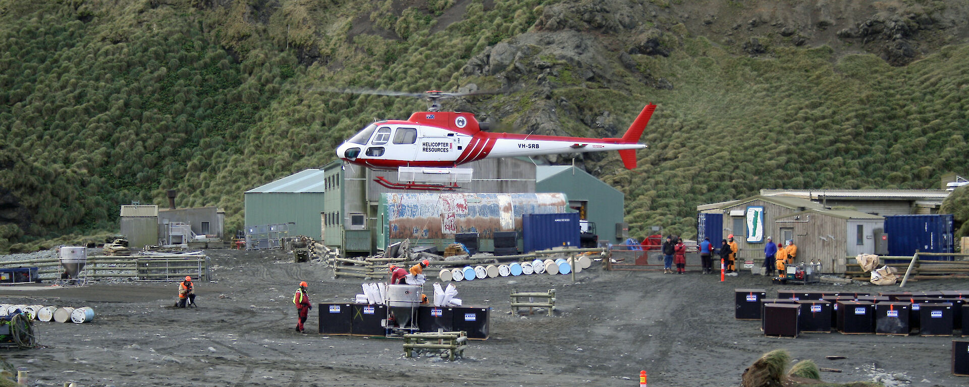 Helicopter taking off near powerhouse with sheds and equipment nearby