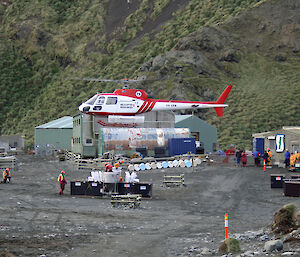 Helicopter taking off near powerhouse with sheds and equipment nearby