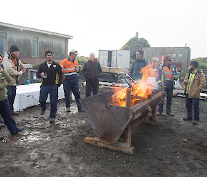 A group of people stand around a fire