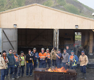 A group of men pose in front of the boatshed