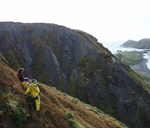 Three expeditioners on a steep slope overlooking the ocean