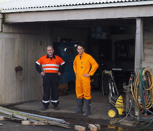 Two men standing outside a mechanical shed in high vis outfits.