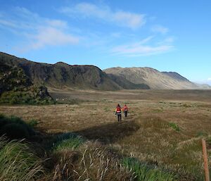 Two people walking with mountains in the background.