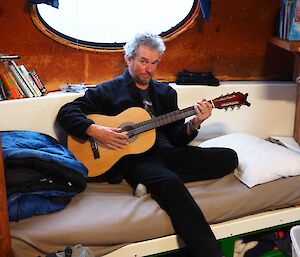 A man sitting on the couch playing a guitar.