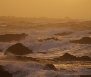 A very yellow sunset over the water with some rocks poking out.