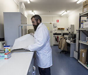 Man wearing white coat examining large piece of filter paper