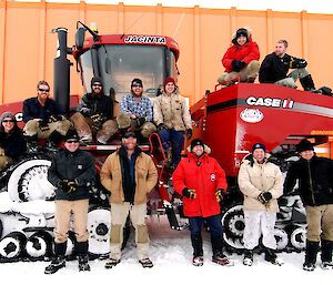 A group of expeditioners standing and sitting in front of a very large tractor.