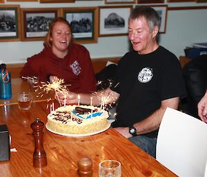 Two people sitting at a table with a birthday cake in front of one of the expeditioners.