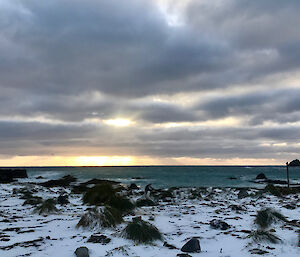Snow on the ground at sunset looking out to sea.