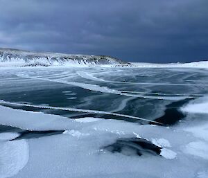 A frozen lake with snow on the surrounding hills.