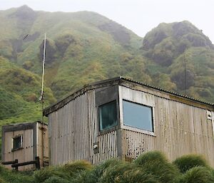 A wooden hut with hill behind it.