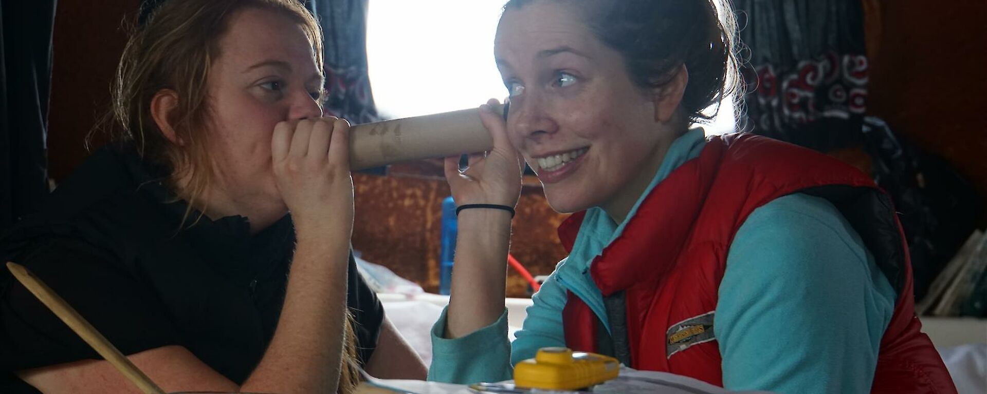 Two expeditioners using a cardboard roll as a telephone, joking about.