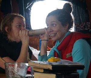 Two expeditioners using a cardboard roll as a telephone, joking about.