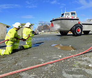 Two expeditioners squirting a fire hose at a vehicle.