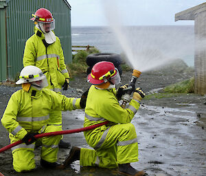 Three people in fire fighting outfits squirting a hose.