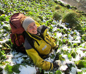 A woman sitting in the vegetation wearing a heavy backpack.